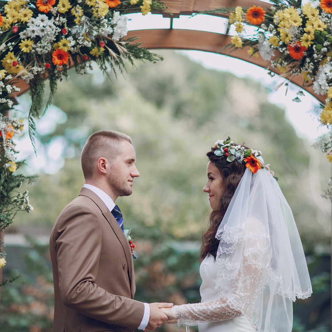 bride and groom holding hands during their ceremony under a wooden arch decorated with flowers.