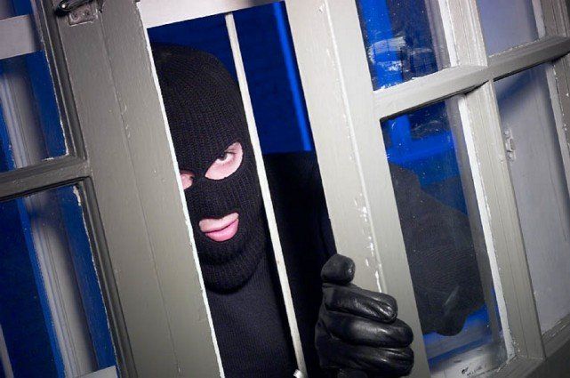 Einbrecher mit Maske blickt durch eine leicht geöffnete Tür