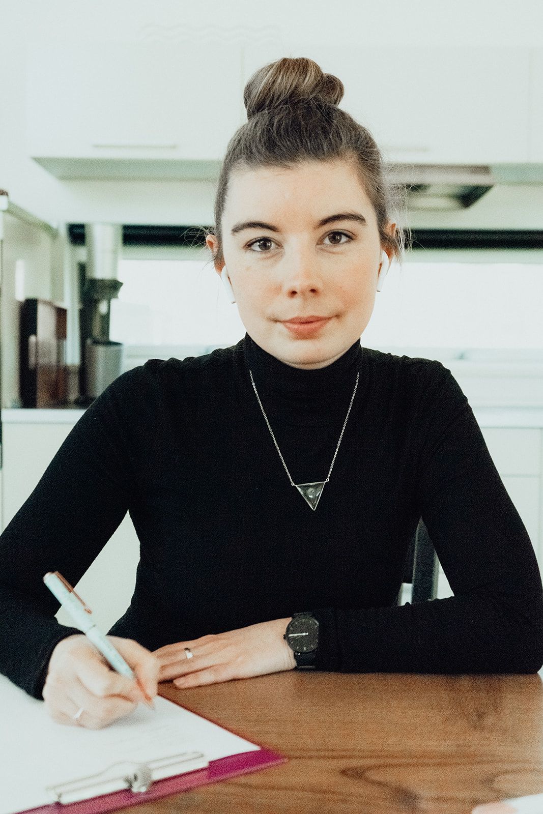 Lisa Holtmeier sitzt am Tisch und hat einen Stift in der rechten Hand und ein Klemmbrett auf dem Tisch.
