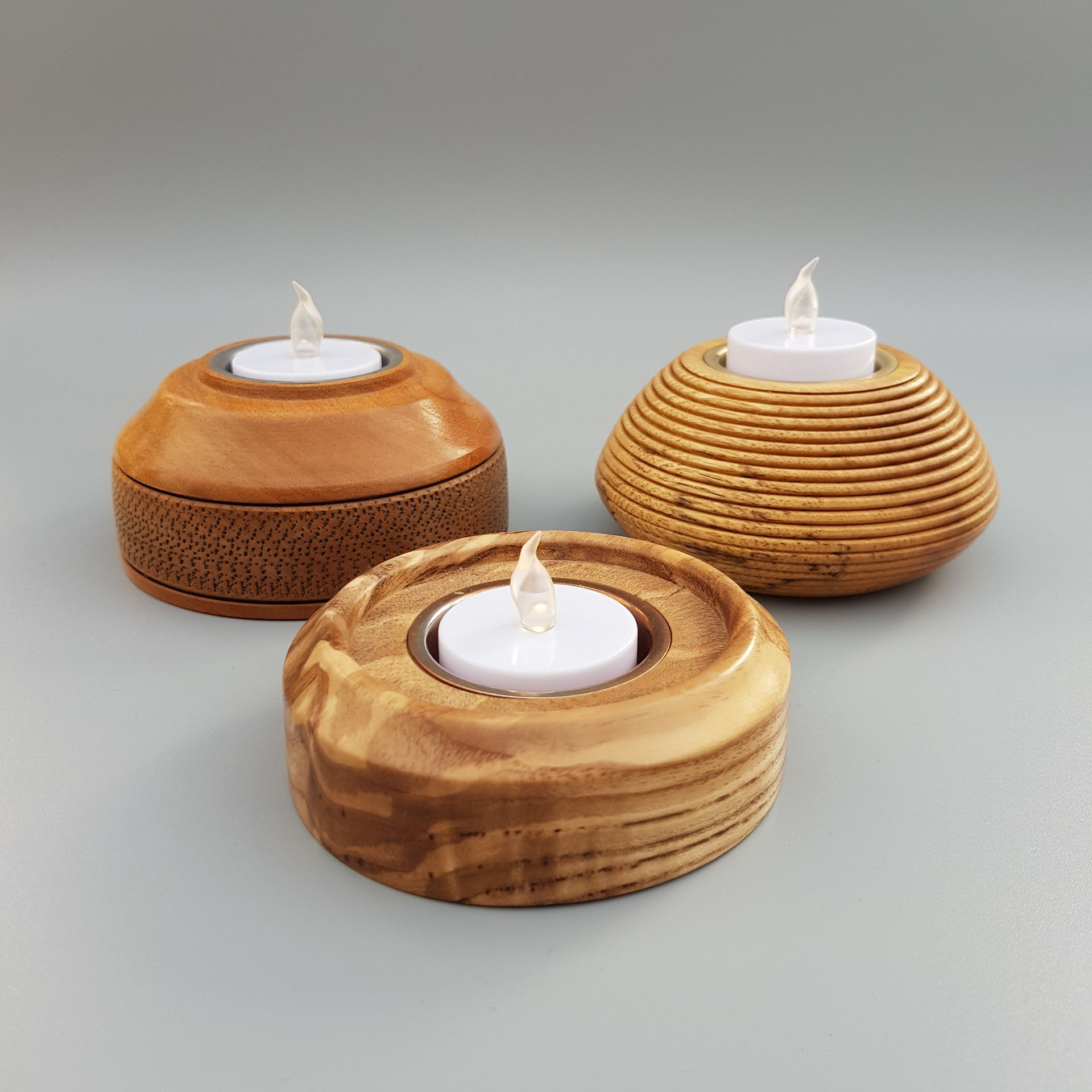 Three wooden tealight holders in various wood on a pale grey backdrop.