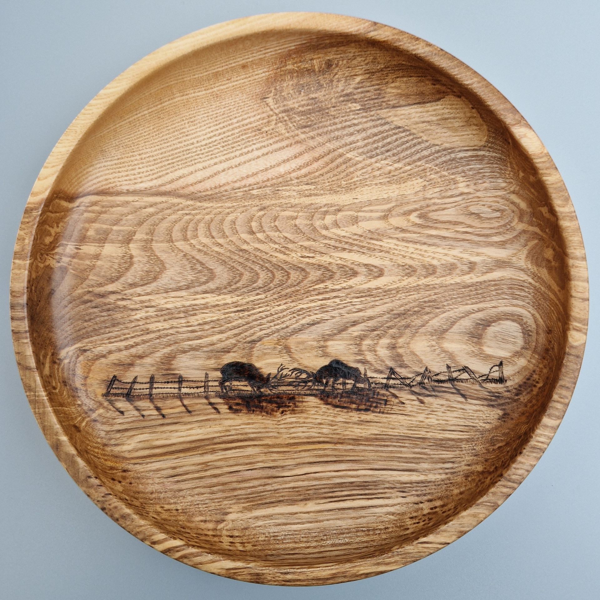 Pyrographed Wood burning art image of two stags locking antlers in a rut, on an ash wood bowl with a dramatic grain pattern which provides the perfect back drop to the pyrography.