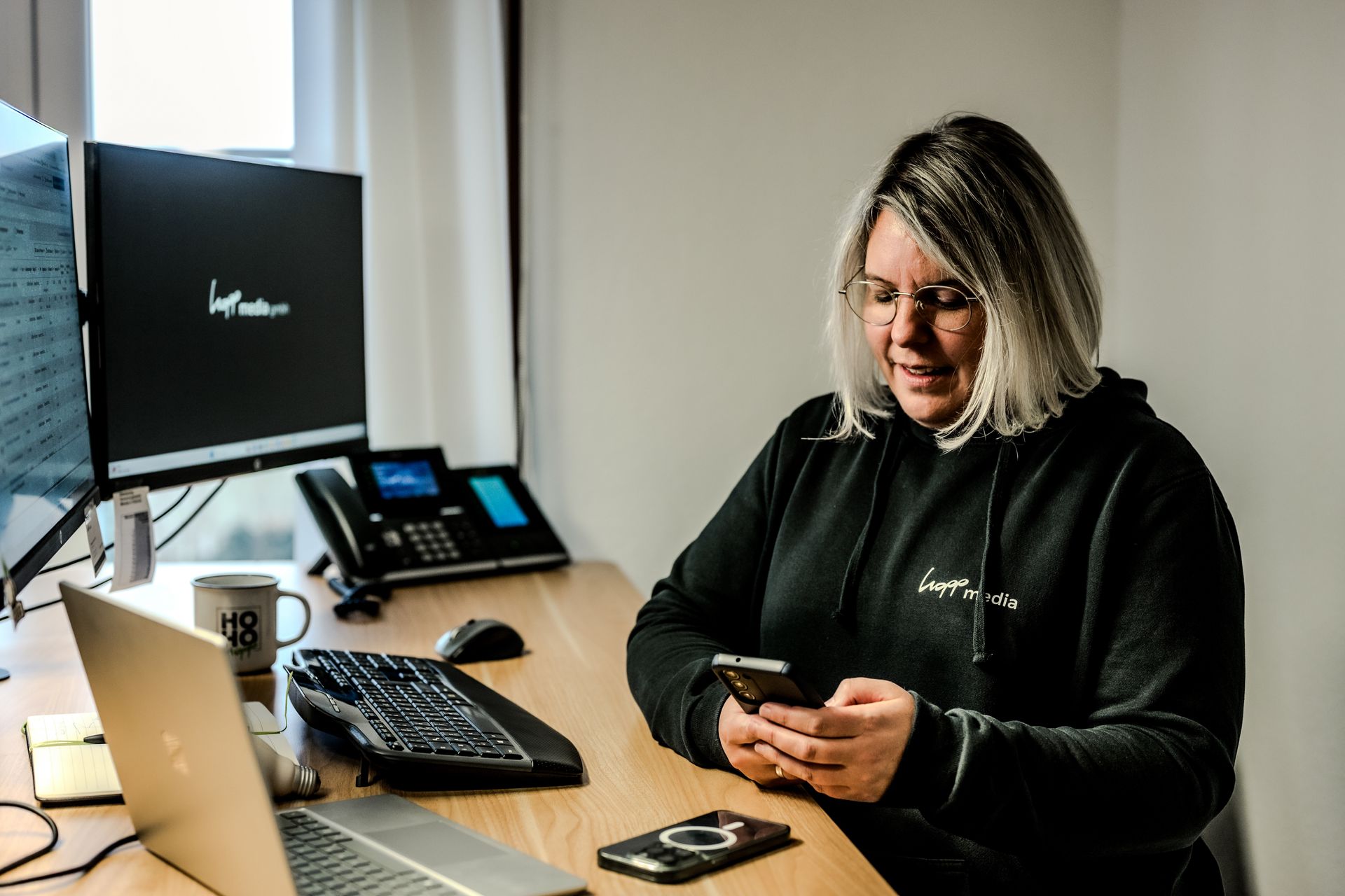Eine Frau, die an Ihrem Schreibtisch sitzt und im Smartphone die neuesten Social Media Strategiene recherchiert und analysiert.