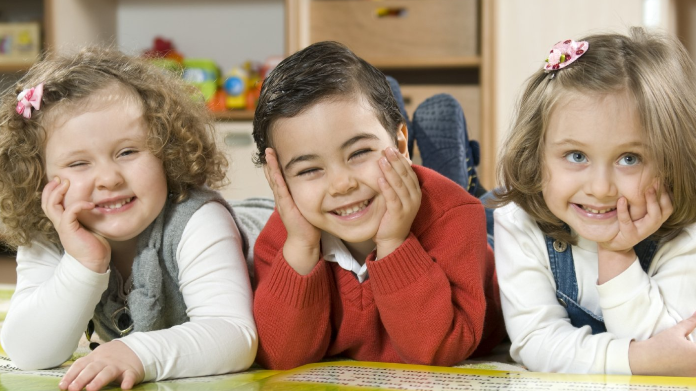 Symbolbild Das Symbolbild zeigt 3 Kinder, die auf dem Boden liegen und grinsen