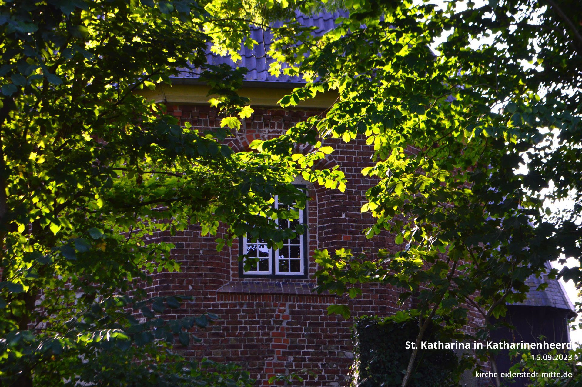 Das Bild zeigt den Blick vom Parkplatz durch Bäume auf die östliche Kirche.