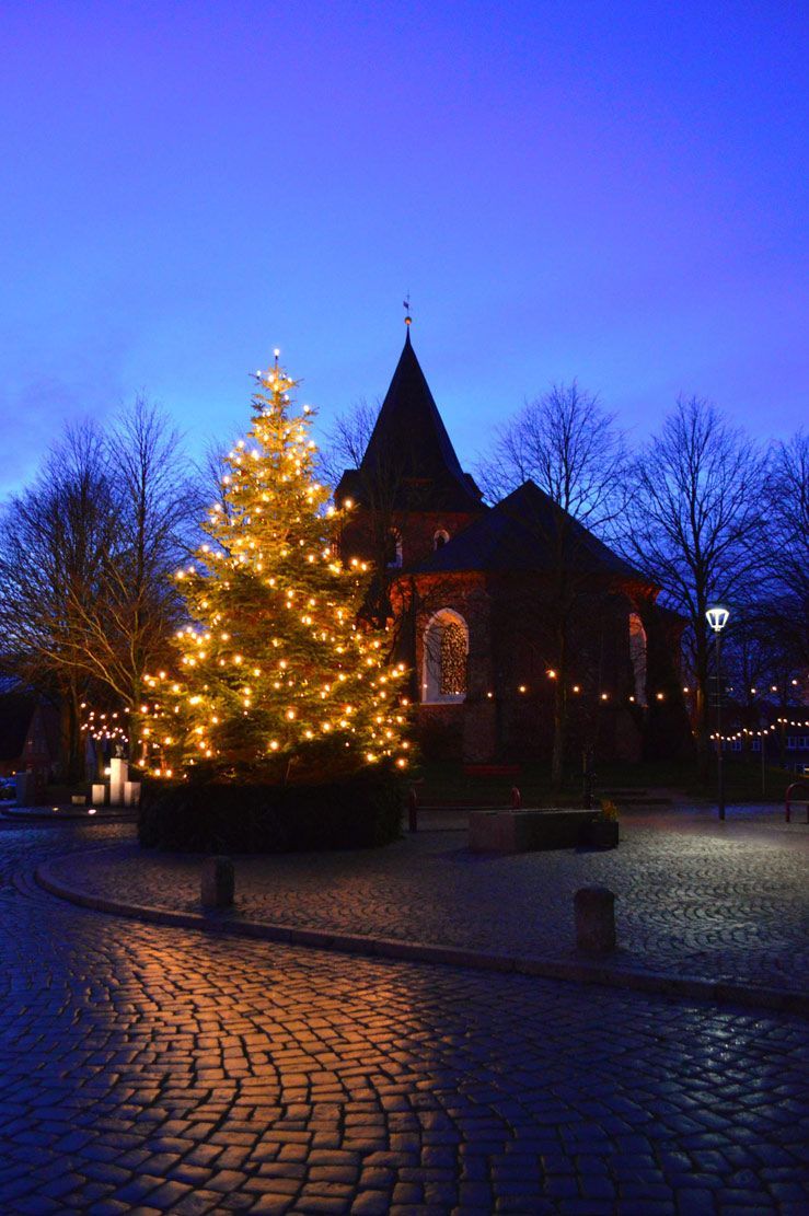 Das Bild zeigt die Kirche St. Christian zur Weihnachtszeit. Im Vordergrund ein leuchtender Weihnachtsbaum.