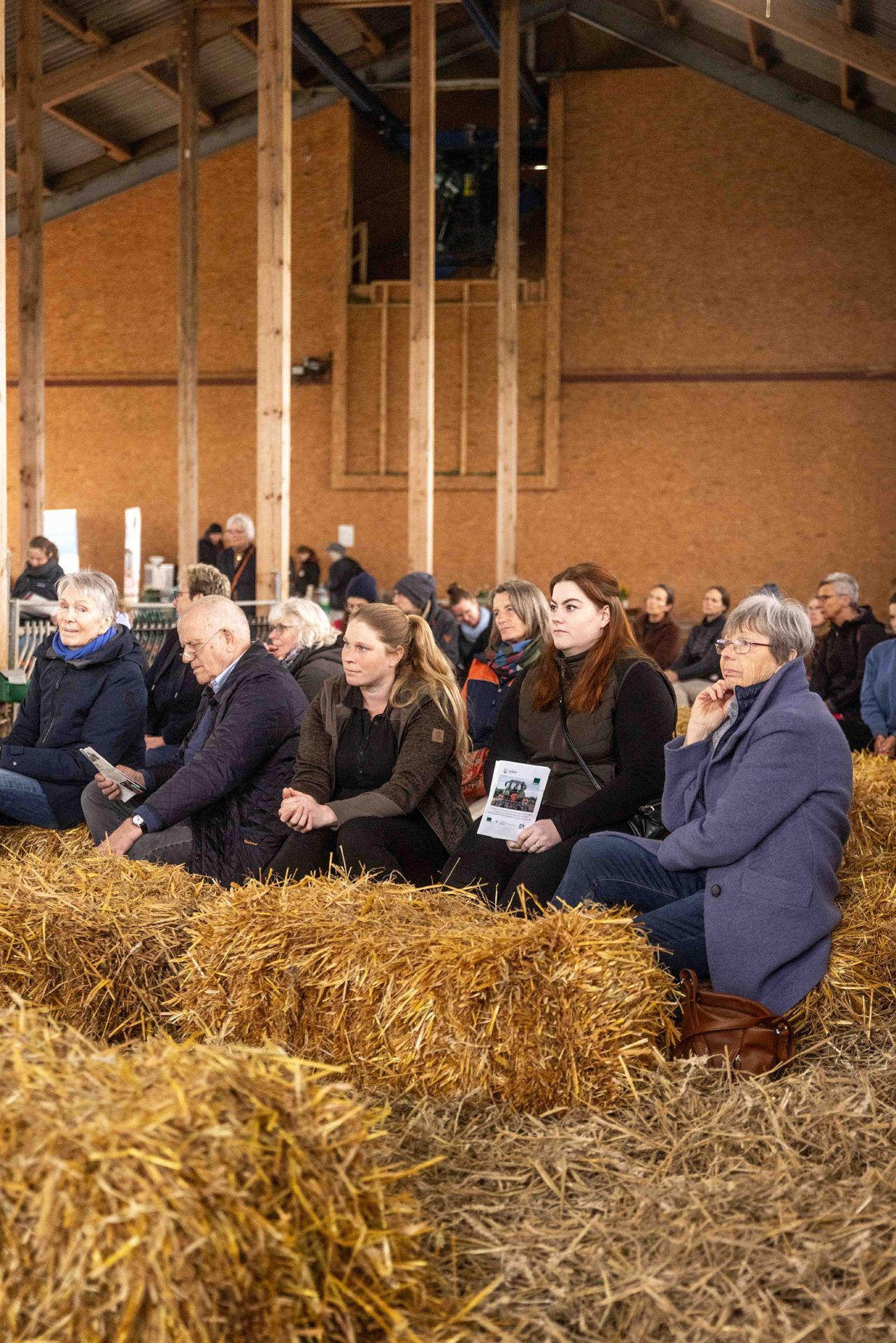 Gemeindemitglieder sitzen auf Heuballen und hören die Andacht