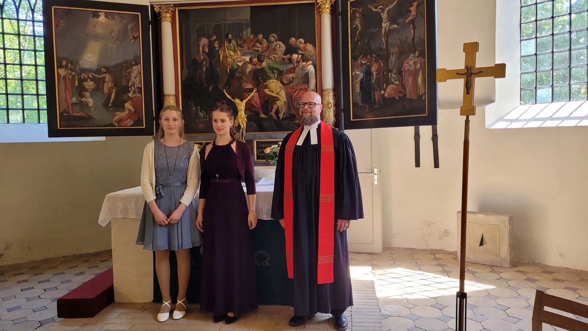 2 Konfirmandinen stehen mit dem Pastor vor dem Altar