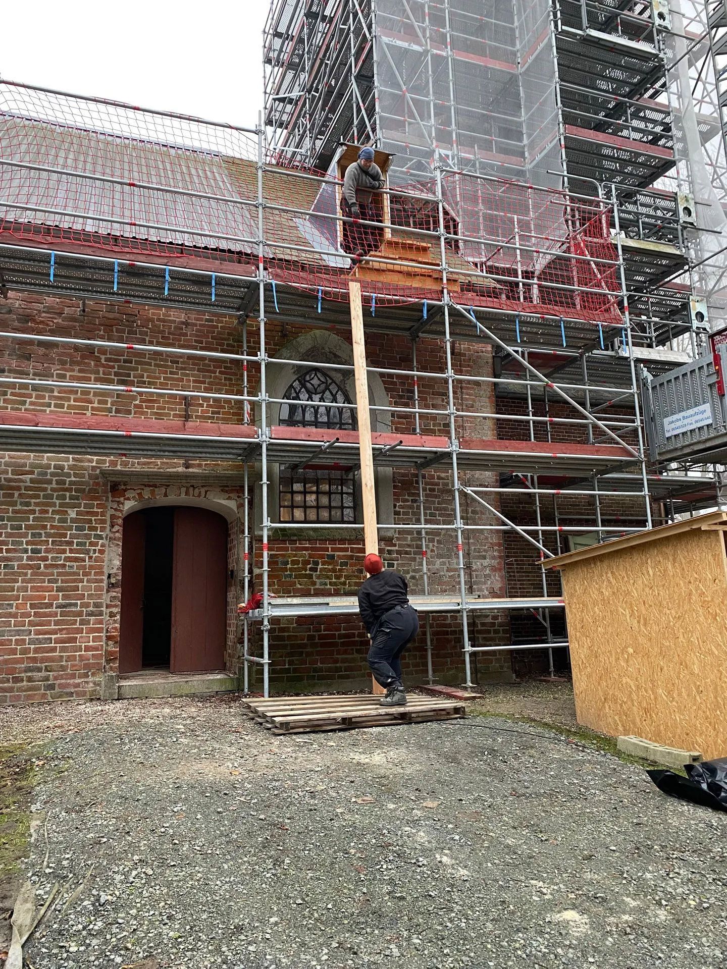 Eine Handwerkerin reicht am Turmgerüst ein Brett nach oben