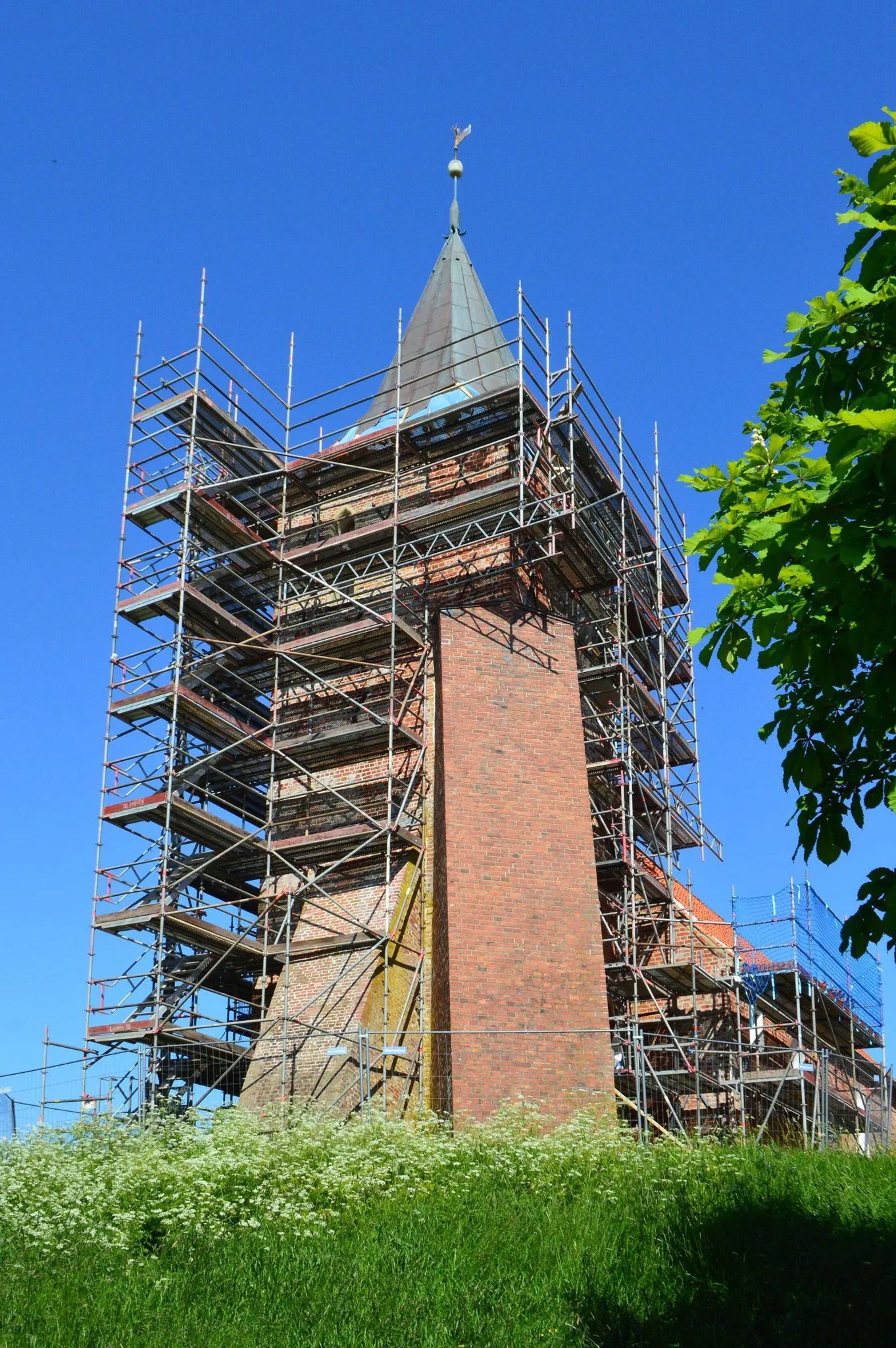 Das Bild zeigt den Kirchturm mit einem Baugerüst aus westlicher Ansicht