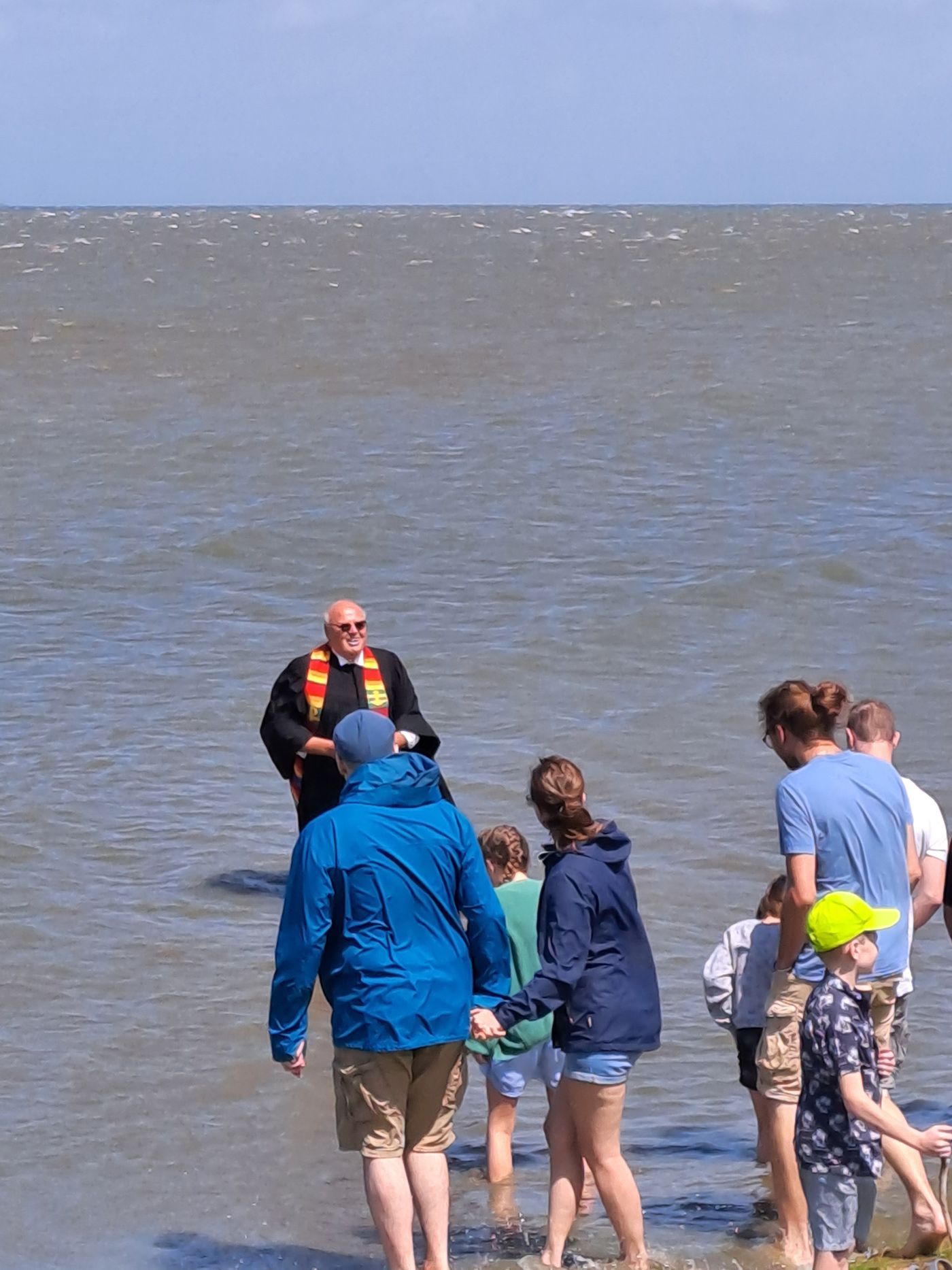 Das Bild zeigt die Deichtaufe in Stufhusen in Westerhever mit Pastor Knippenberg. Der Pastor steht im Nordseewasser.