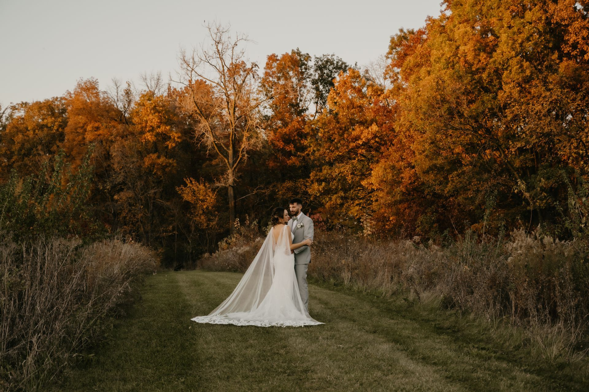 Bride and groom pose at Fort Wayne wedding venue Union 12 with fall treeline backdrop and scenic outdoor setting.
