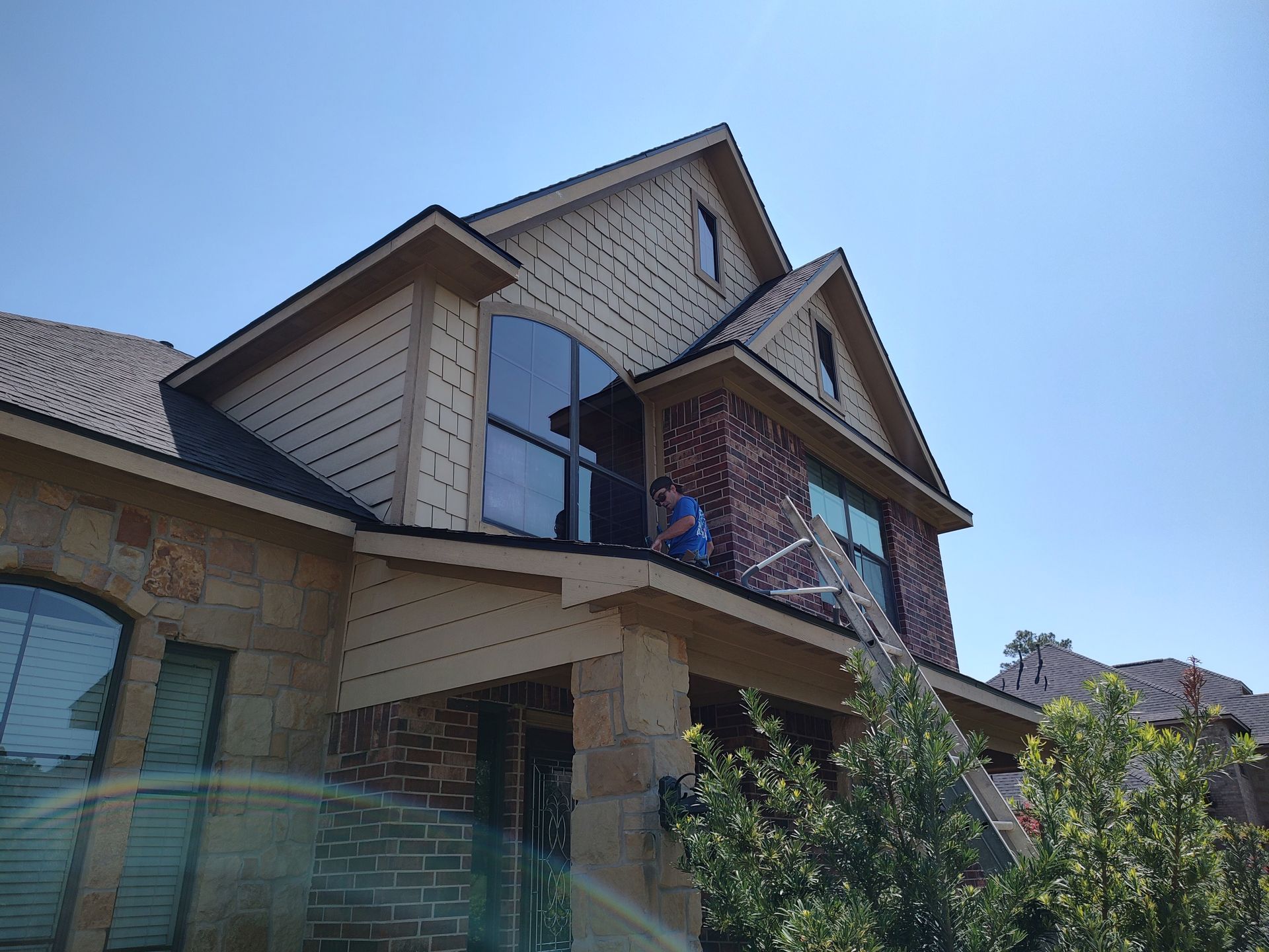 All Git Out Services team member cleaning a second-story window while safely positioned on a porch roof.