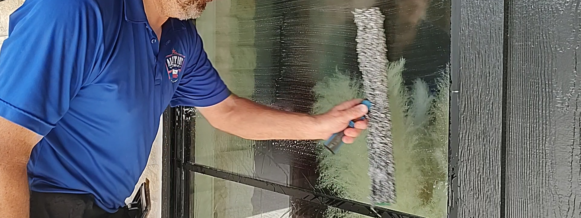 A close-up of a premium microfiber mop saturated with professional soap thoroughly soaking a residential window pane to loosen surface dust and create a protective lubricated barrier