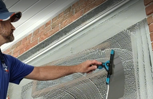 Achieving a crystal-clear finish: All Git Out Services removing water from a large window with a professional squeegee.
