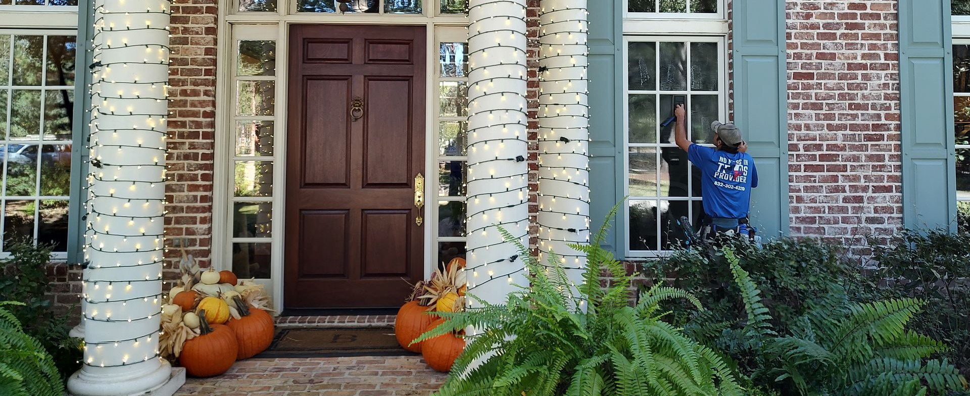 A beautifully decorated Magnolia, Texas home entrance featuring white pillars surrounded by autumn pumpkins at the base, showcasing clean front windows ready for the fall holidays.