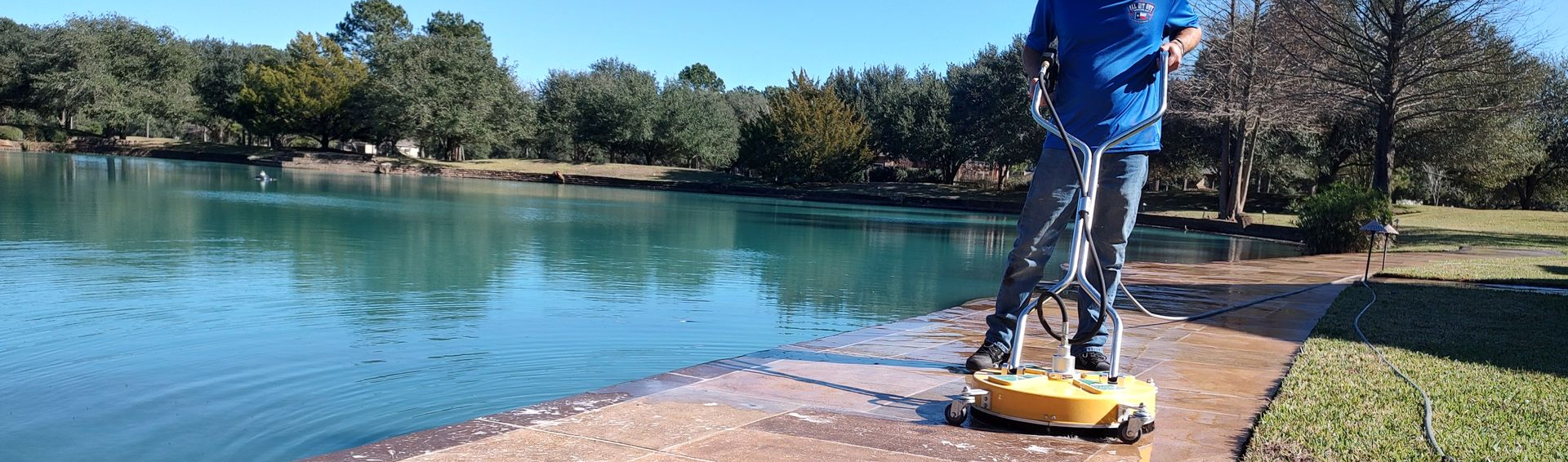 Professional surface cleaner being used by a specialist to clean and restore a stamped concrete walkway near a pond on a property in Waller, Texas.