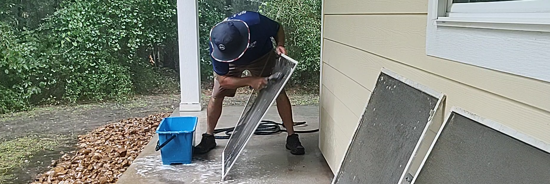 Scott Glander of All Git Out Services deep-cleaning a residential mesh window screen to remove pollen, dust, and spider webs before reinstallation.