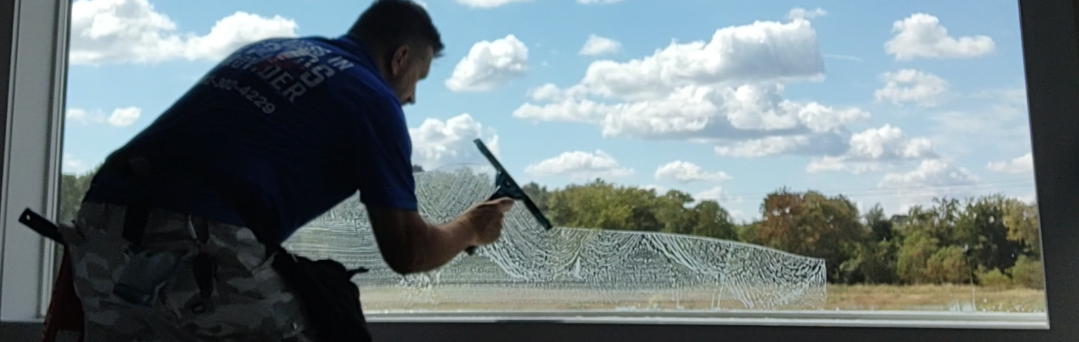A window cleaning specialist using a traditional squeegee to hand-wash a large residential window to a flawless, streak-free shine.