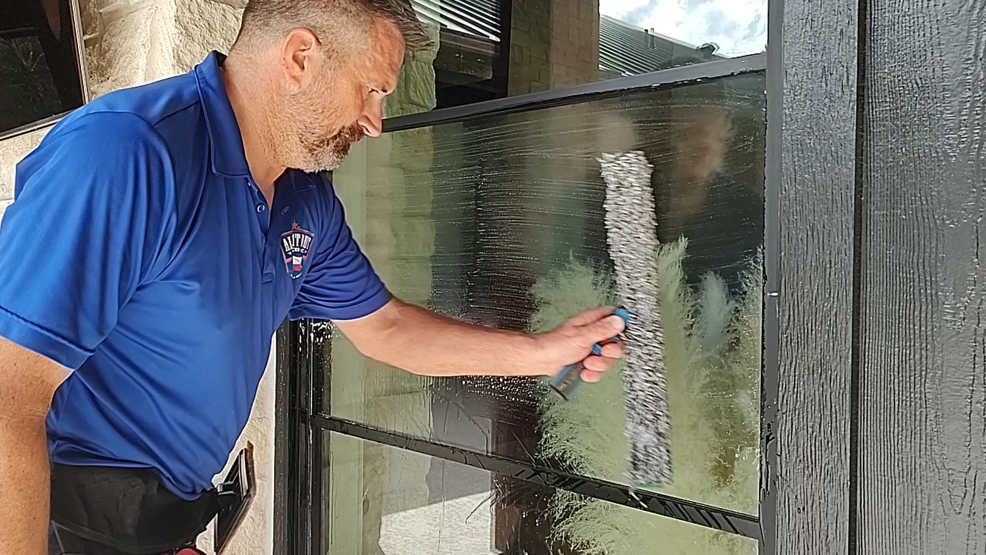 A professional window cleaning specialist applies a special cleaning solution with a mop during a hand-wash service.