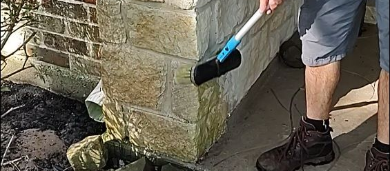 applying bleach with a soft brush on a stone veneer pillar to remove the algae that extra detail we do when soft washing