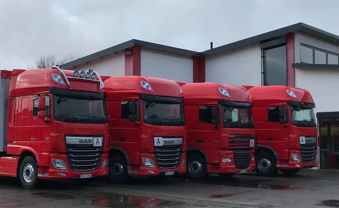 4 rote DAF- Sattelzugmaschinen vor dem VELOG Bürogebäude