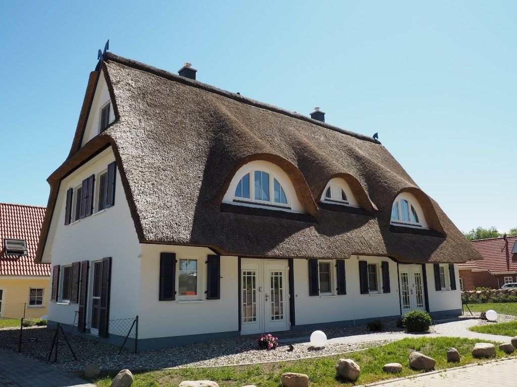 Sie suchen ein strandnahes und extravagantes Feriendomizil, um im Kreise Ihrer Familie, mit Freunden, Kollegen oder mit Ihrem Partner die Seele baumeln zu lassen? Dann haben wir die richtigen Ferienhäuser für Sie! Unsere Ferienhäuser sind exklusiv, komfortabel und mit viel Liebe zum Detail im Landhausstil eingerichtet. Sämtliche Räumlichkeiten sind hell und freundlich gestaltet. Jedes Haus hat ein eigenes Farbkonzept und verfügt über: einen Kaminofen, mind. 2 Bäder mit bodengleichen Duschen (davon ein Wellnessbad mit zusätzlicher Badewanne), hauseigene Sauna, Fußbodenheizung, Fliegenschutz (in Bädern und Schlafräumen), hochwertige Matratzen, Verdunkelung (in Schlafräumen), eine hochwertige und vollausgestattete Einbauküche, Safe, SAT-TV, WLAN, Fahrradschuppen und vielem mehr. Den naturbelassenen Strand (Abgang Teufelsschlucht) erreichen Sie fußläufig. Der Strand lädt zum Sonnenbaden, zu romantischen Spaziergängen oder ausgedehnten Wanderungen ein. Der Küstenwald oberhalb der Steilküste spendet im Sommer Schatten und am Abend haben Sie die Möglichkeit auf zahlreichen Bänken den Sonnenuntergang über der Ostsee zu genießen. Alternativ können Sie auf der Sonnenterrasse am Haus im Kreise der Familie oder mit Freunden bei einem guten Glas Wein den Tag ausklingen lassen. Uns ist wichtig, dass unsere Gäste eine entspannte An- und Abreise haben. Sollten Sie frühzeitig gebucht haben, senden wir Ihnen Ihren individuellen Zugangscode zum Feriendomiziel per Post zu. Auf Wunsch senden wir Ihnen ebenso Ihre Kurkarte. Das bedeut für Sie: Keine zusätzlichen Wege, keine Einhaltung von Öffnungszeiten. Ankommen und sich wohlfühlen! Während der Hauptsaison empfehlen wir Ihnen, nicht samstags an- und/oder abzureisen, wir bieten unseren Gästen daher insbesondere den Freitag und Sonntag als An- und Abreisetag an. Dies hat für Sie den Vorteil, dass die Verkehrslage voraussichtlich etwas entspannter ist. Ihr Urlaub könnte aber natürlich auch am Samstag beginnen und/oder enden. Gut erzogene Vierbeiner auf Anfrage. Aber bitte: Textilien, Lederecke sowie Betten sind für Ihren Liebling tabu! Wir haben nur Nichtraucherhäuser im Programm! Holzkohle und offenes Feuer sowie Feuerwerkskörper sind aufgrund der Brandgefahr der Reetdächer nicht gestattet!.