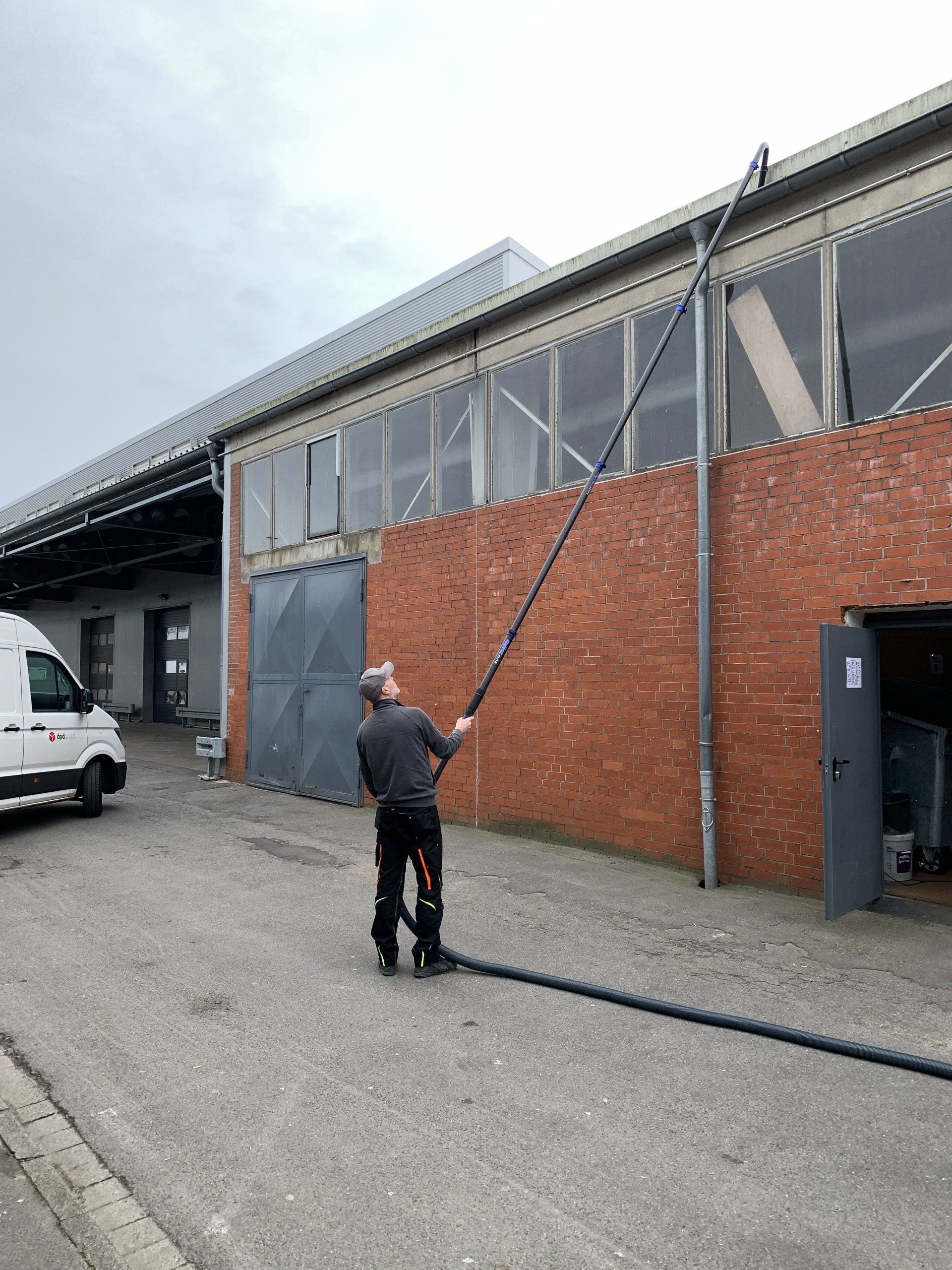 Ein Hausmeister reinigt die Dachrinne mit Skyvac