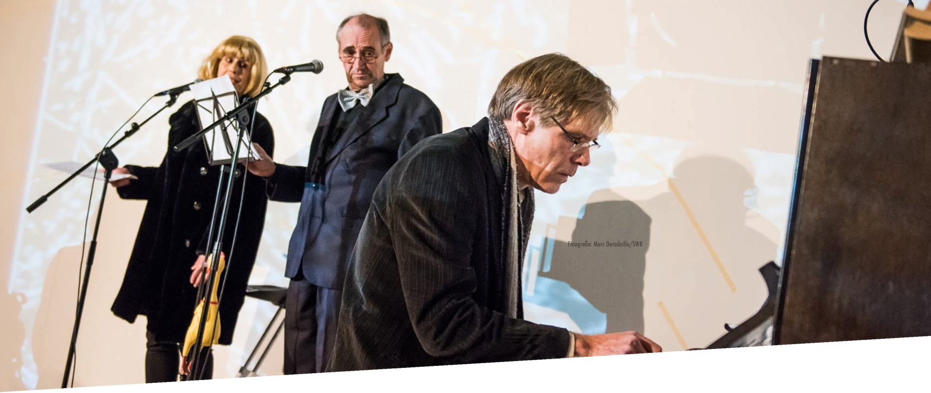 Ein Mann am Klavier, zwei Personen hören zu