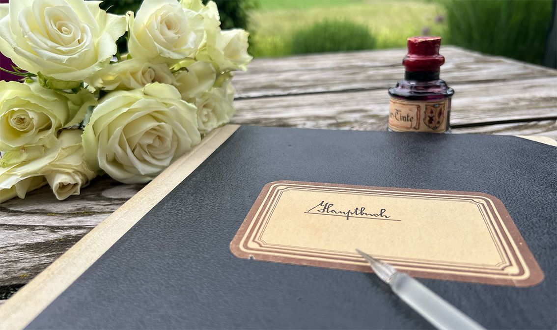 Ein altes Kassenbuch, gefüllt mit Zahlen in alter Schreibschrift, Rosen und ein Tintenfass.