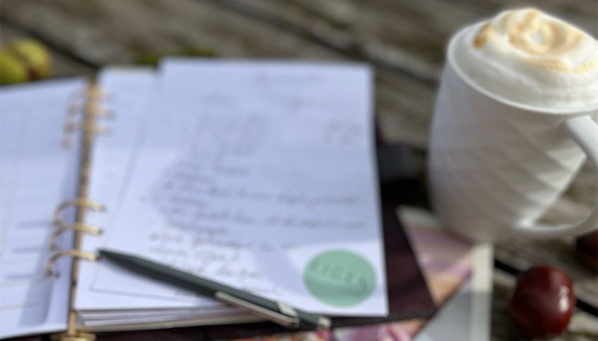 Ein Tasse mit Cappuccino, ein Kalender mit einer langen To-Do-Liste, ein Stift, Arbeitsorganisation