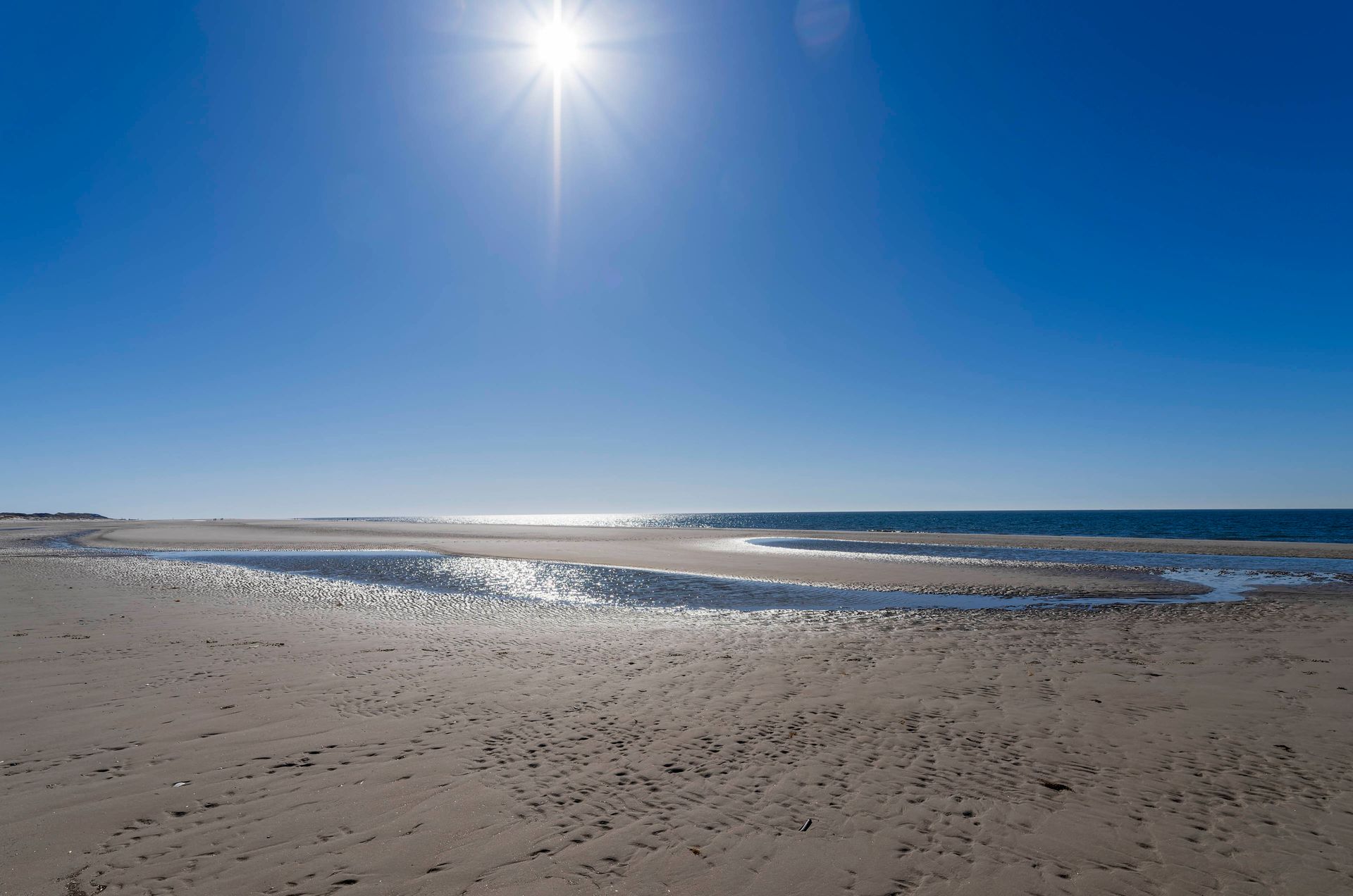 Reflexionen au nassem Sand im Gegegnlicht Strand mit Wasser im Sandbereich bei Gegenlicht, Sonne im Bild einbezogen