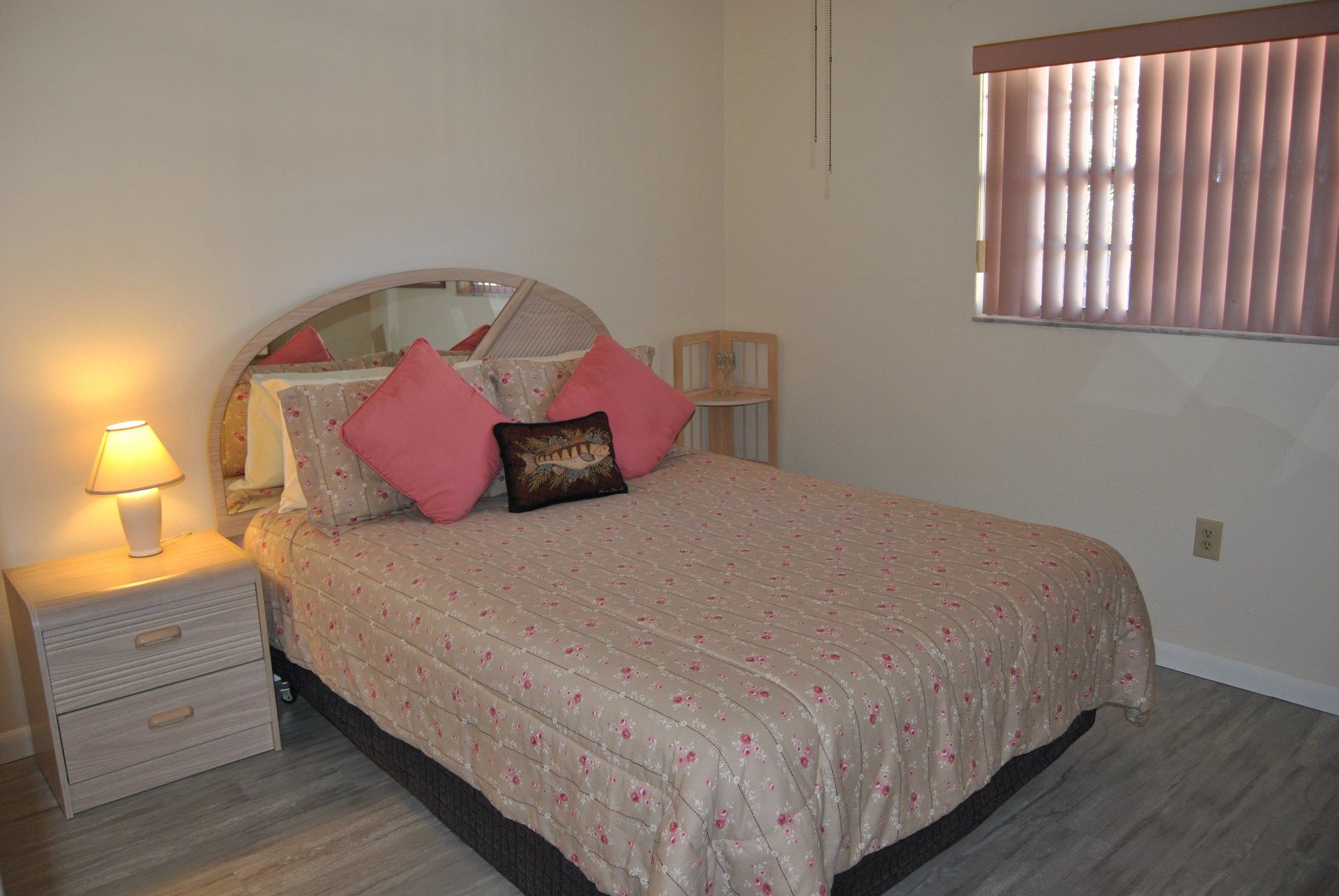 Full size bed with flowered cover, side table, pink shades