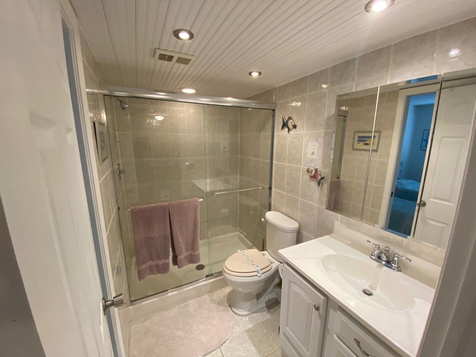 Beige fully tiled bathroom with tub, glass shower doors,toilet, sink with mirrors