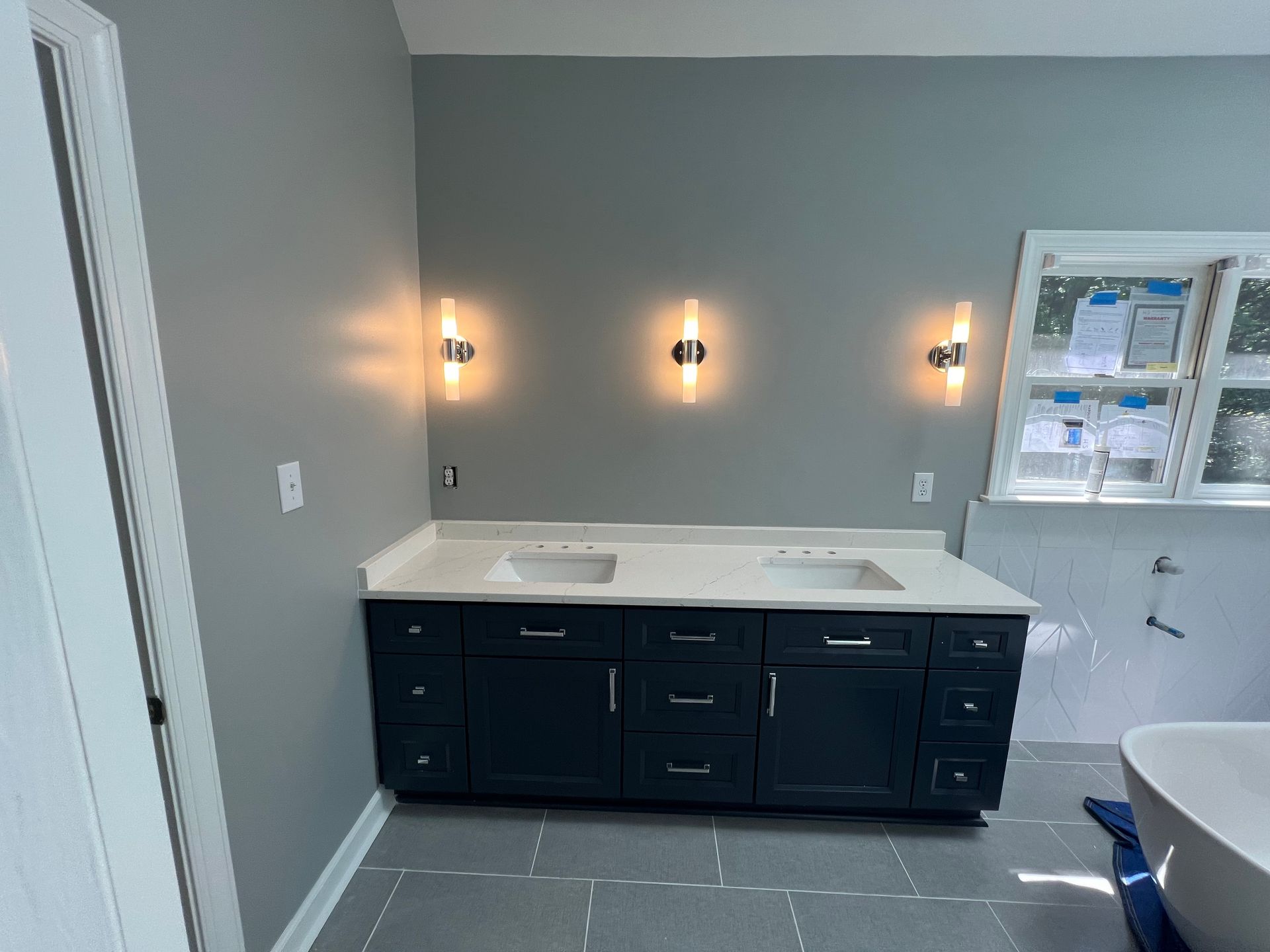 Double vanity bathroom lighting upgrade with three matte black wall sconces above mirrors – Rolesville, NC.