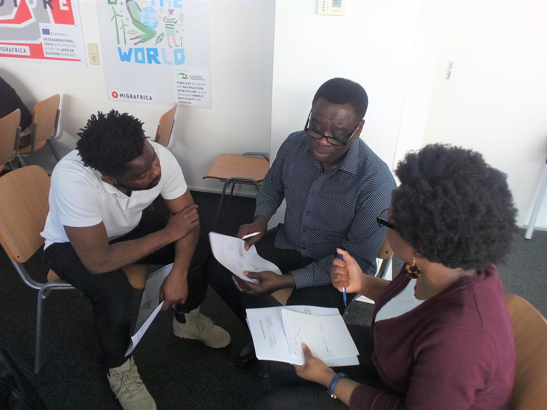 Drei afrikanisch gelesene Erwachsene sitzen in einem kleinen Stuhlkreis und unterhalten sich - Projekt Dialog Afrika