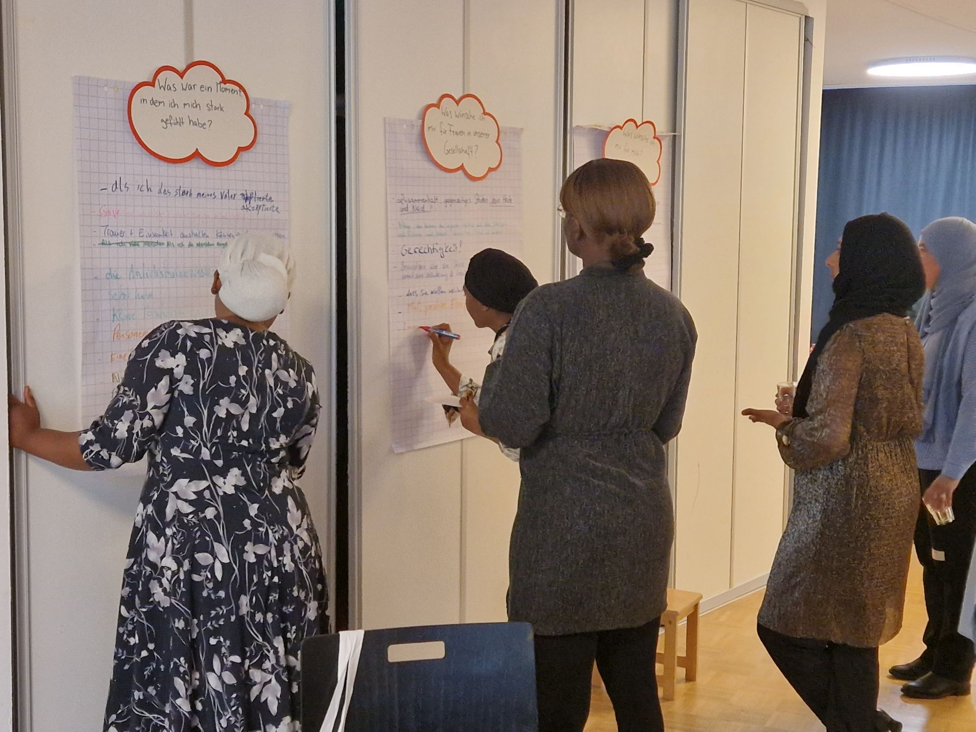 Teilnehmerinnen von Her Diversity beschreiben Flipchart-Blätter, die mit unterschiedlichen Fragen an der Wand hängen