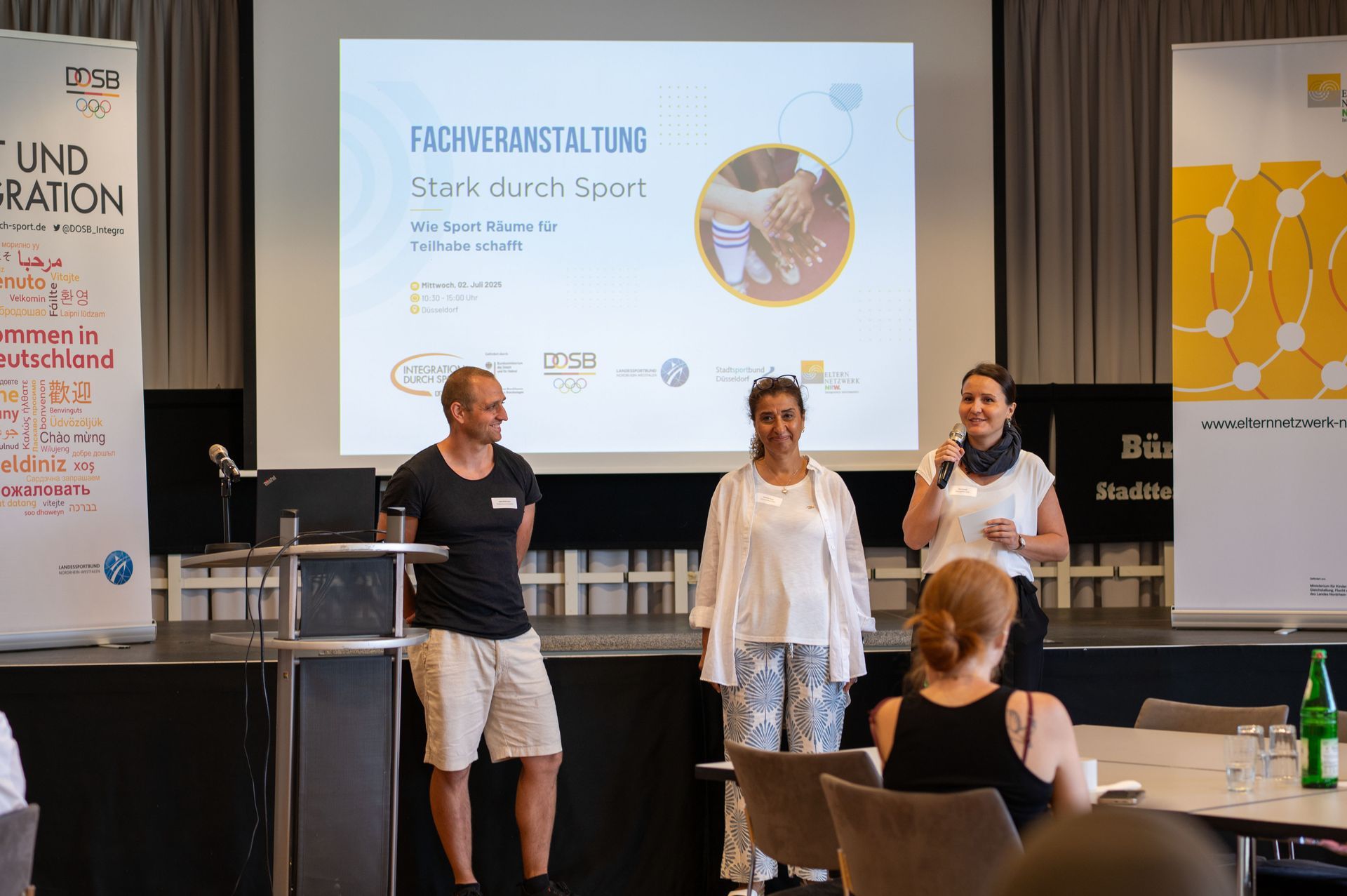 „Stark durch Sport – Wie Sport Räume für Teilhabe schafft“ - Drei Referent:innen vor dem Publikum, Evan Cynkar am Mikrofon