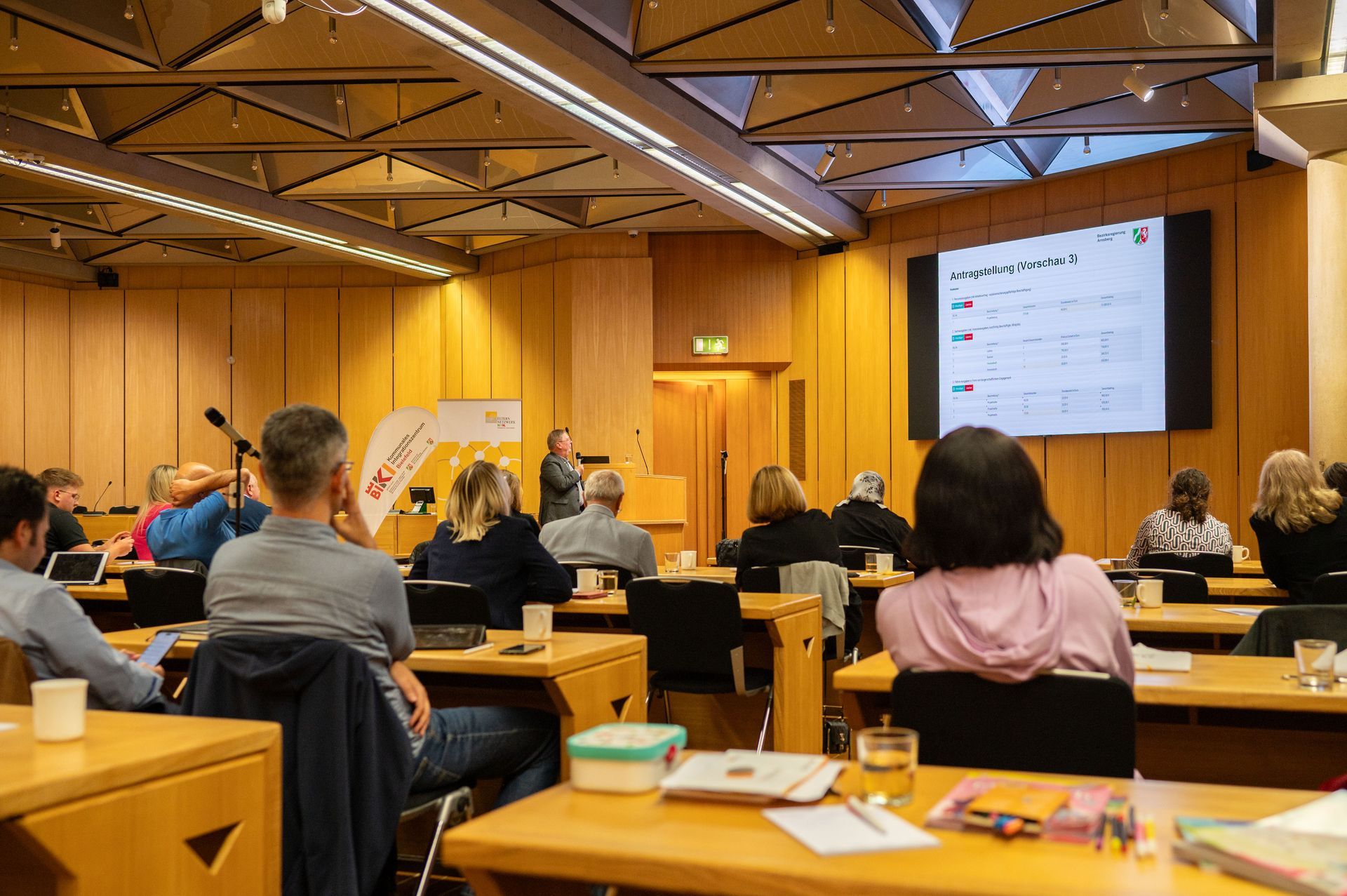 Informationen zur Antragsstellung werden den an Tischen vor der Präsentation sitzenden Teilnehmenden gegeben