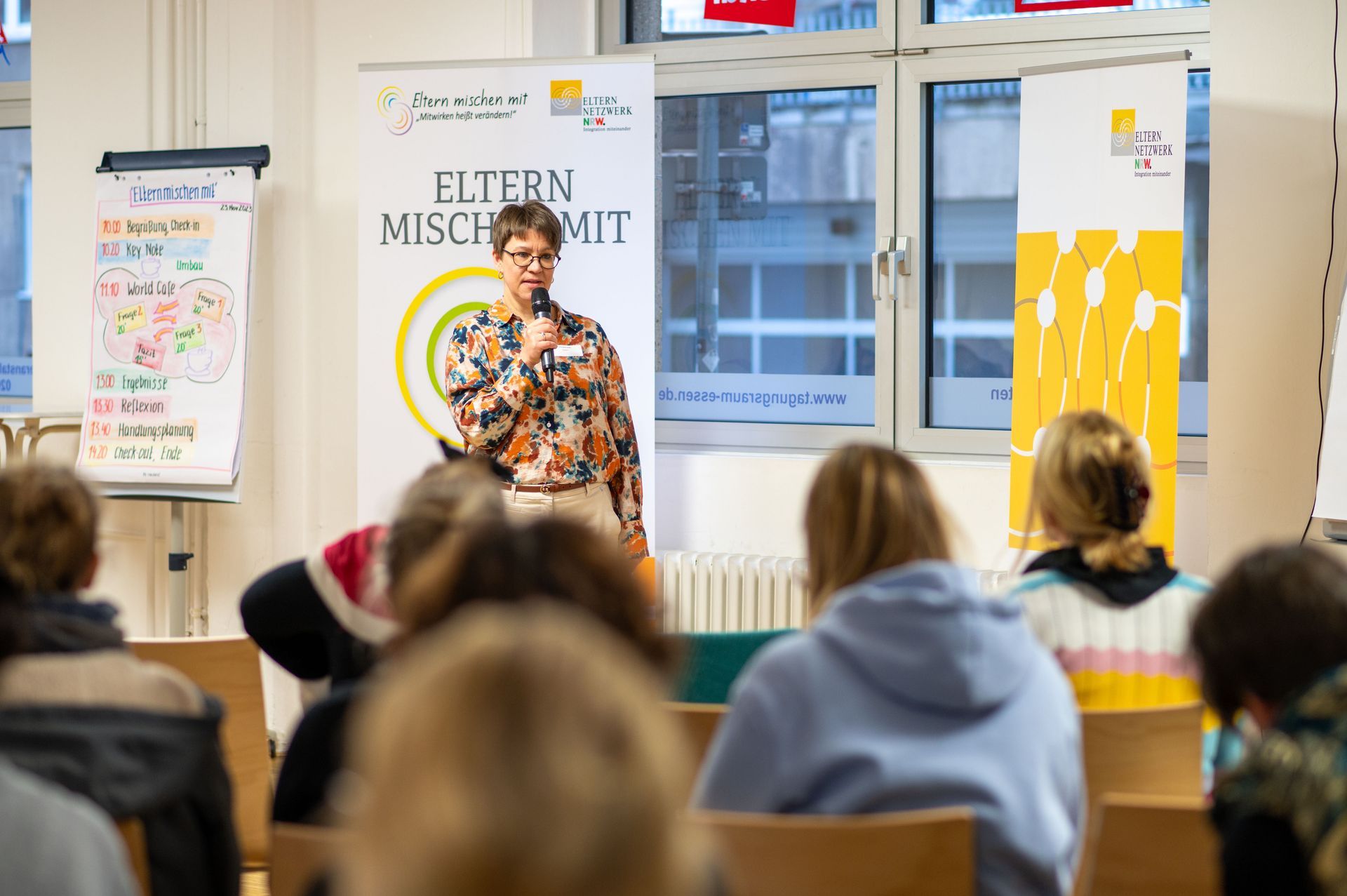 Frau Sonja Gierse-Arsten steht vor Banner des Projekts Eltern mischen mit und spricht zu Teilnehmer*innen.
