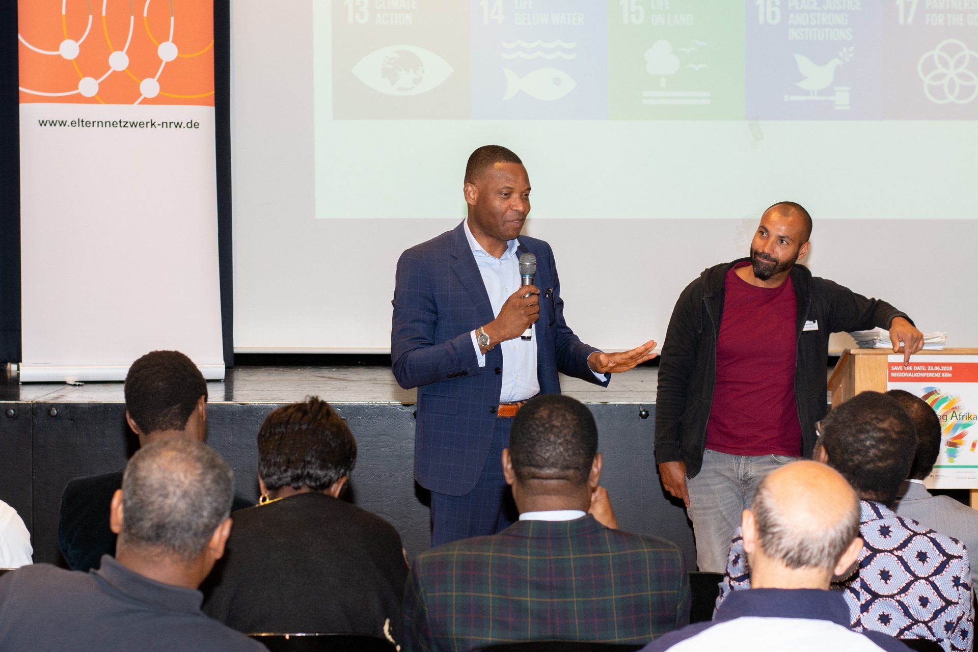 Eli Abeke (sitzt im Integrationsrat der Stadt Köln für Bündnis14 Afrika), Serge Palasie (Eine-Welt-Netz NRW e.V) vor Publikum