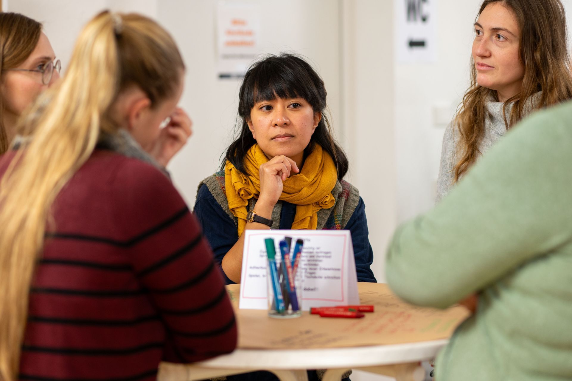 Aubrey Fabay, Mitarbeiterin im Projekt Eltern msichen mit schaut nachdenklich. Am Tisch Teilnehmerinnen der FA.