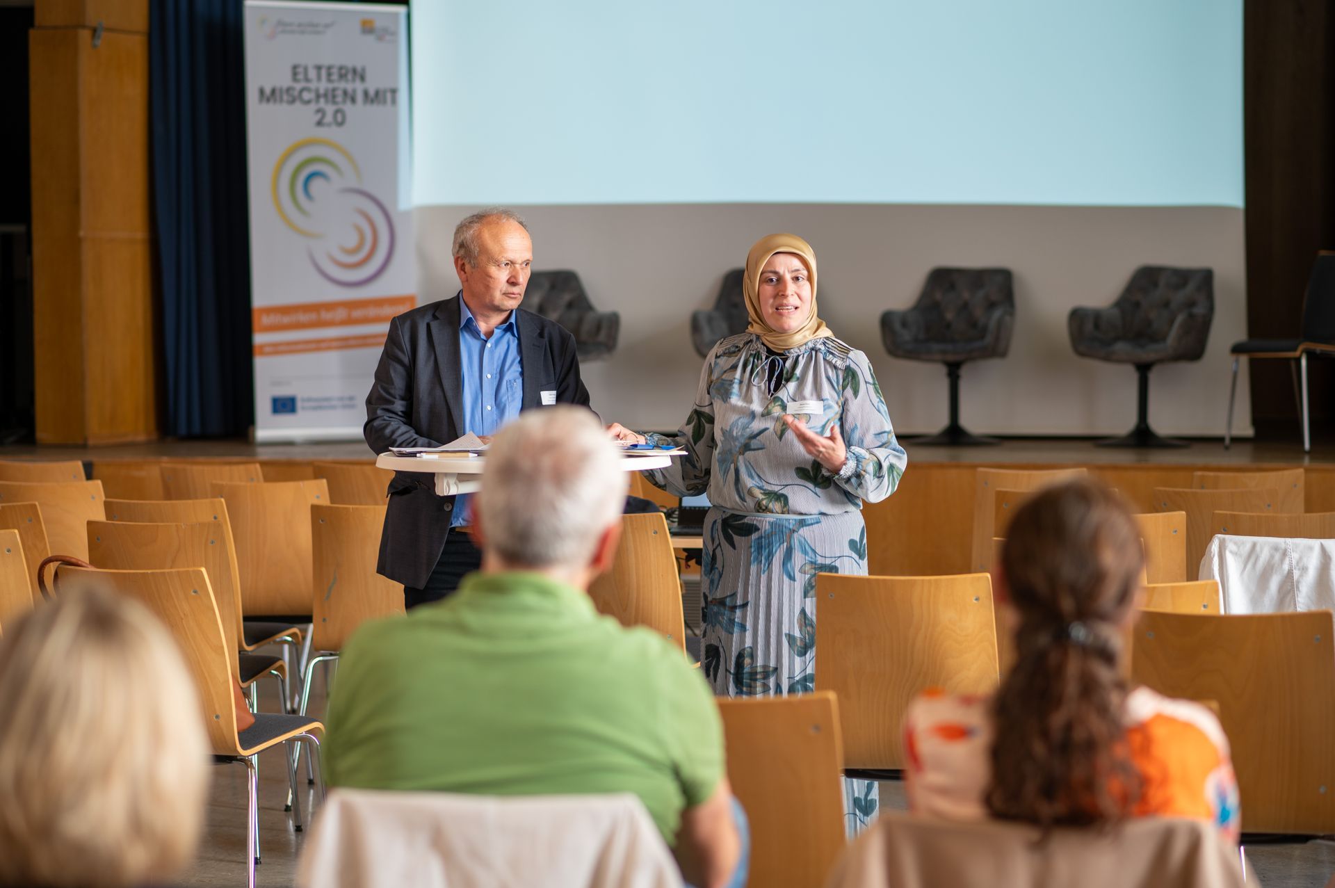 Workshop Leitende stehen vorne und unterhalten sich mit Teilnehmenden in den Stuhlreihen