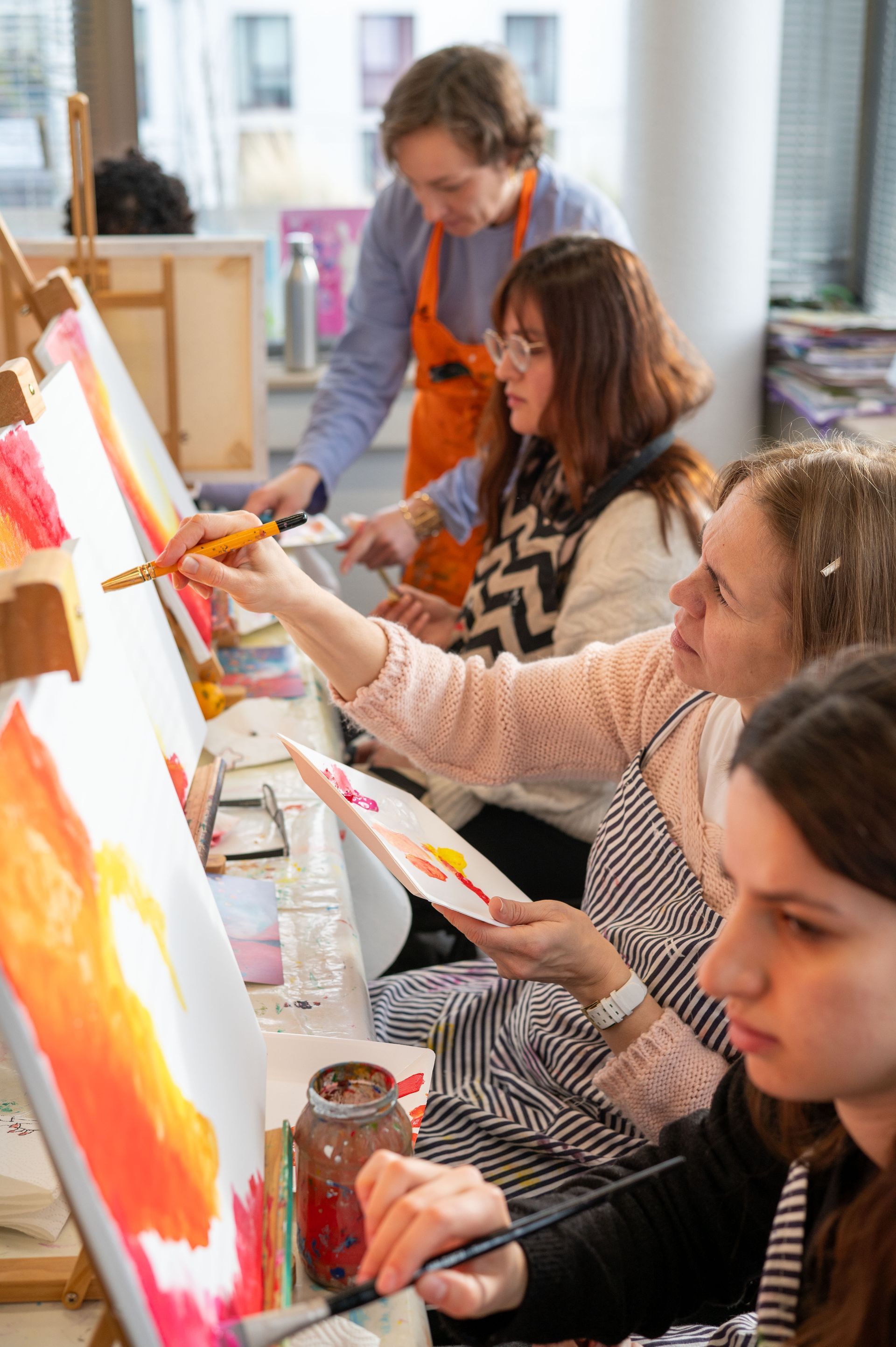 Her Diversity Frauen, die am Tisch sitzen & mit Pinseln ihre Leinwände mit kräftigen Farben bemalen.