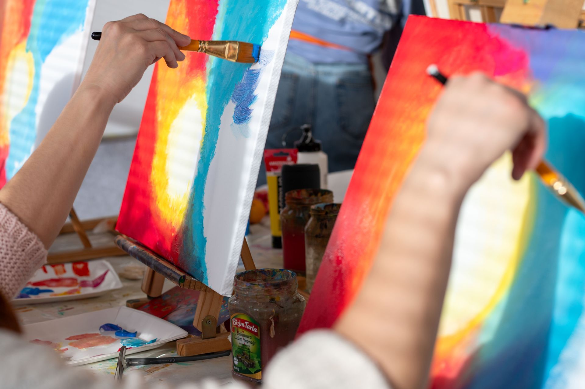 Mehrere Hände malen farbenfrohe abstrakte Bilder auf Leinwänden in einem kreativen Workshop.