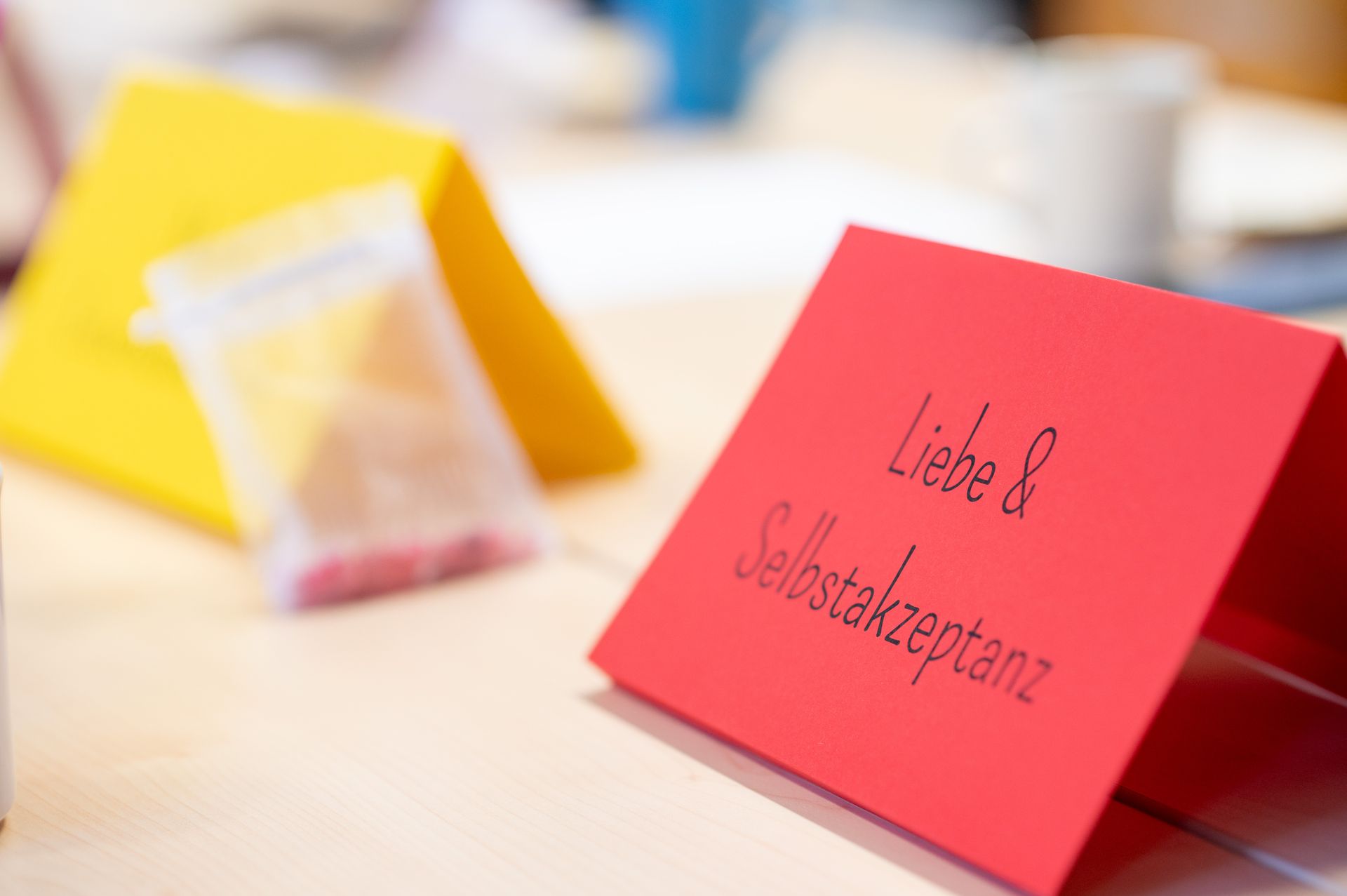Gelbes und ein rotes Aufstellkärtchen stehen auf einem Tisch. Auf dem roten steht