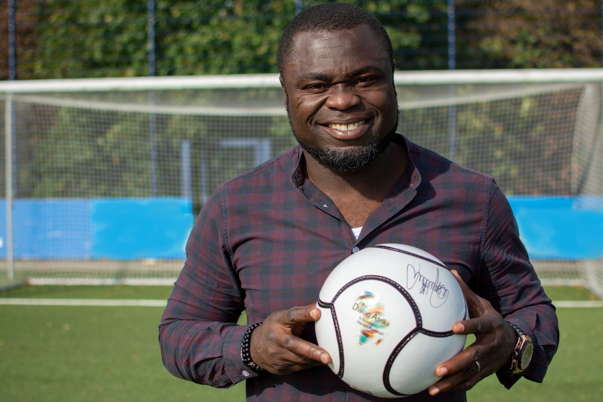 Schirmherr des Projekts Dialog Afrika Gerald Asamoah mit Fußball in der Hand auf dem Fußballplatz
