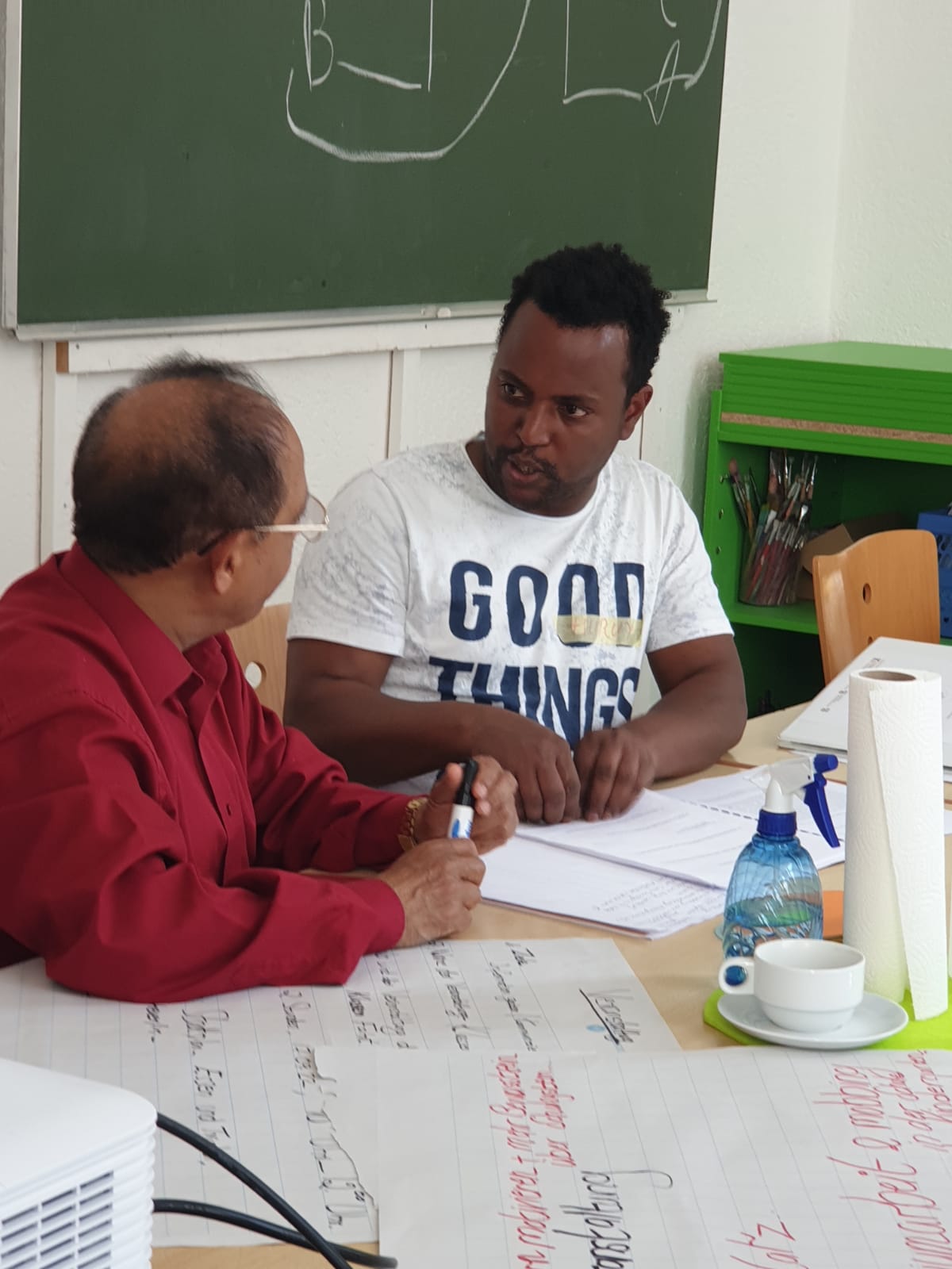 Zwei Männer kommen durch das Projekt Eltern mischen mit ins Gespräch. Im Hintergrund eine Schultafel.