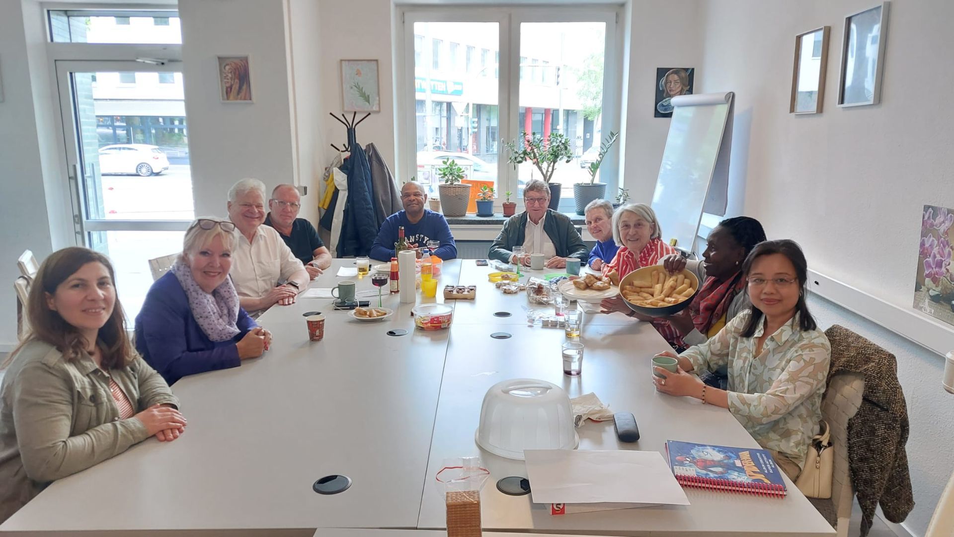 Menschen verschiedener Generationen sitzen an einem Tisch, trinken Kaffee und sprechen miteinander.