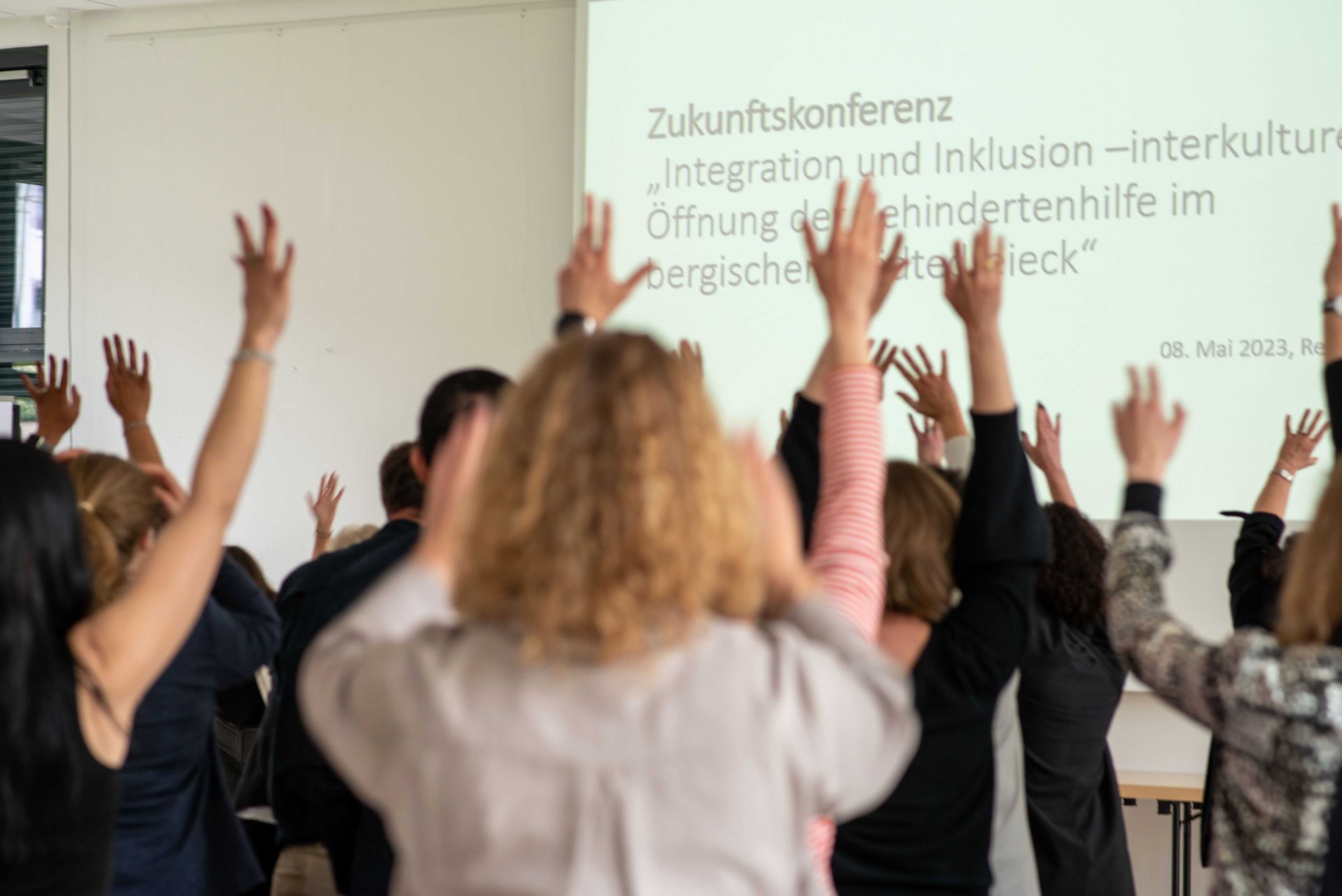 Rückenansicht ins Publikum, die die Hände heben bei der Zukunftskonferenz. Link führt zu Projektseite Kultur Inklusiv II