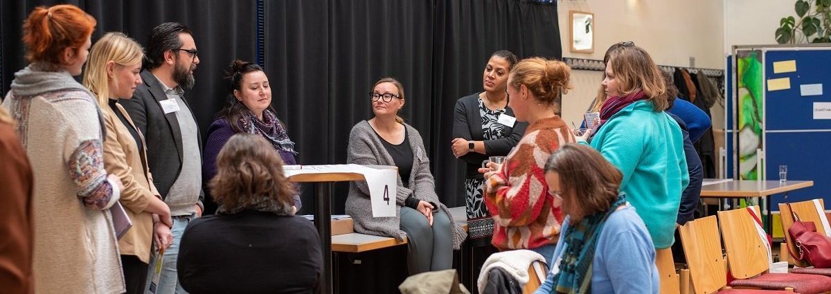 Mehrere Teilnehrminnen udn ein Teilnehmer stehen in einem losen Kreiis und unterhalten sich beim Werkstatttreffen